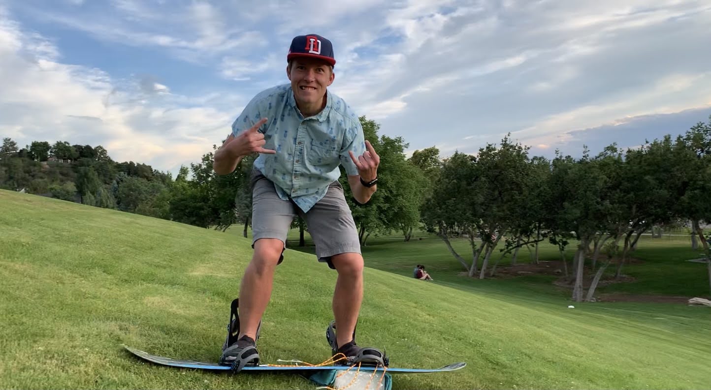 Kamryn is snowboarding on a grass hill with ice on the bottom of his board
